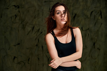 Fototapeta premium Beauty concept, stylish portrait. Photo of a pretty glamorous brunette girl in a black t-shirt with flying hair on a gray fashionable original background.