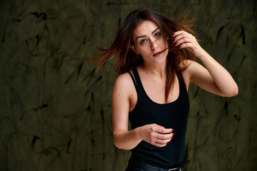 Beauty concept, stylish portrait. Photo of a pretty glamorous brunette girl in a black t-shirt with flying hair on a gray fashionable original background.