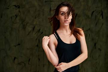 Fototapeta premium Beauty concept, stylish portrait. Photo of a pretty glamorous brunette girl in a black t-shirt with flying hair on a gray fashionable original background.