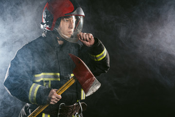 young caucasian handsome and strong fireman in uniform wearing helmet on head hold hammer in hands,...