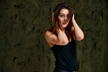 Fototapeta na wymiar Beauty concept, stylish portrait. Photo of a pretty glamorous brunette girl in a black t-shirt with flying hair on a gray fashionable original background.