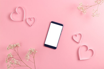 Composition for Valentine's Day February 14th. Delicate pink background, phone and notebook with recognition. A heart cut out of paper. Greeting card. Flat lay, top view, copy space.