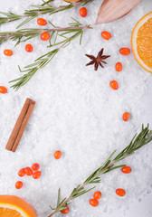 Winter background with artificial snow, sea buckthorn berries, rosemary, cinnamon sticks, orange and star anise. Copy space