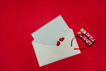 The Concept Of Valentine's Day. Love letter. An envelope, a blank sheet of paper, a gift box and red hearts on a red background. Free space for your text.