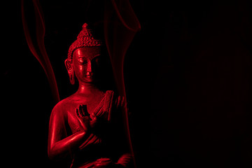 A religious ornamental buddha figure lit by a red flash on a black background with copy space