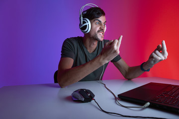 Portrait of an angry gamer playing video games on computer in dark room wearing headphones.