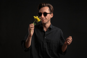 Sexy man in a black shirt and sunglasses holding beautiful yellow flower to give it to his beloved