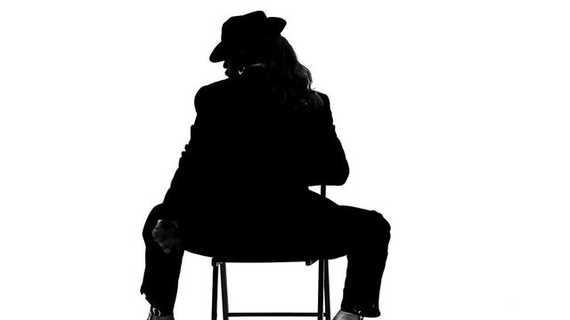 Silhouette Elegant man in a black hat is dancing an erotic dance. He uses a chair and a cigarette. White background. Close up, slow motion.