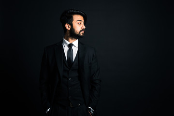 Portrait of a young handsome successful Indian in a classic black three-piece business suit on a dark background