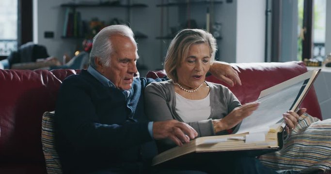 A lovely senior couple is enjoying to watch a photo album with their photo memories on sofa in living room at home.