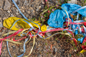 The party is over. Discarded used red, yellow and blue balloons and streamers on gravel ground.