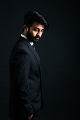 Portrait of a young handsome successful Indian in a classic black three-piece business suit on a dark background