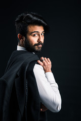 Portrait of a young handsome successful Indian in a classic black three-piece business suit on a dark background, Holding his jacket over his shoulder