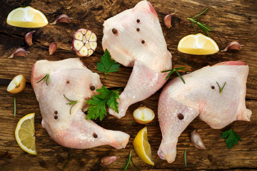 Top view of fresh chicken drumsticks with spices: parsley, pepper, allspice and rosemary on a wooden vintage board.