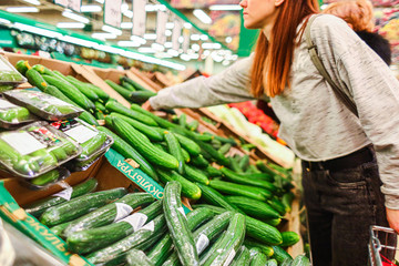Shopping at the supermarket. The girl in the store picks cucumbers in the vegetable department. A healthy and balanced diet.