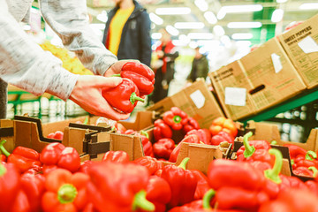 Shopping at the supermarket. The girl in the store chooses peppers in the vegetable department. A healthy and balanced diet.