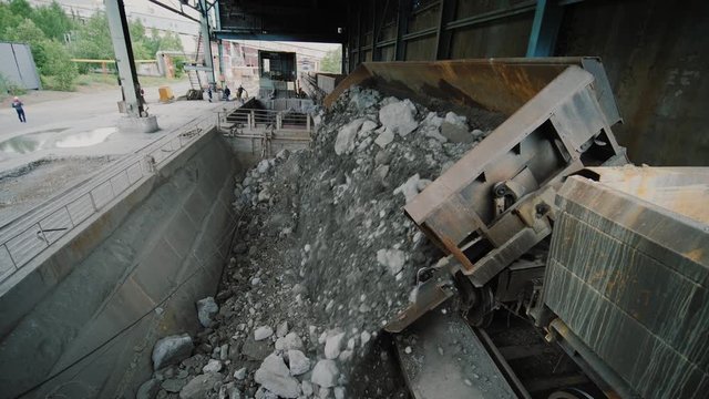 Rail car wagon dumps iron or copper pyrite ore for processing and mining of non-ferrous metals on plant. Freight train dumps minerals for for grinding on factory Quarry and mining equipment.