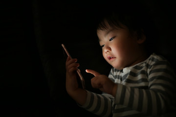 暗い中でスマートフォンを使う男の子