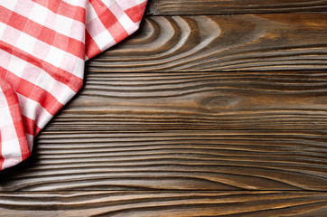 Red checkered napkin on brown wooden kitchen table with copy-space. Top view