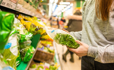 Shopping at the supermarket. The girl in the store chooses a salad in the vegetable department. A healthy and balanced diet.