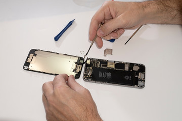 An open phone is on the table. Phone repair in a service center. Screws are unscrewed with a screwdriver tool. Analysis of the battery and matrix.