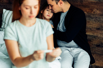 young woman in t-shirt checking thermometer, going to treat from illness kid girl. father hugging supporting sick child in the background, health and medicine concept