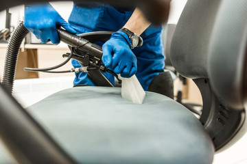 Fototapeta premium Young man in workwear and rubber gloves cleans the office chair with professional equipment.