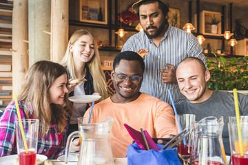 Obraz premium A company of multicultural young people in a cafe eating pizza, drinking cocktails, having fun