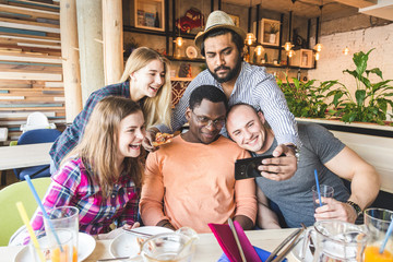 A company of multicultural  young people in a cafe eating pizza, drinking cocktails, having fun