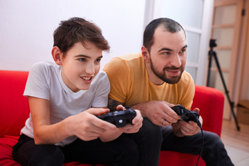 friendly father playing video games with little kid boy, his son. cheerful and happy parent and son playing with joysticks