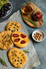 mini focaccia with olives, tomatoes, rosemary, pepper on parchment and gray background
