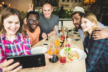 Group of young cheerful friends are sitting in a cafe, eating, drinking drinks. Friends take selfies and take pictures.