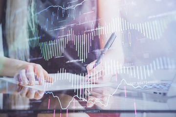 A woman hands writing information about stock market in notepad. Forex chart holograms in front. Concept of research.