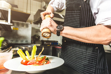 Professional chef cooking in the kitchen restaurant at the hotel, preparing dinner. A cook in an apron makes a salad of vegetables and pizza.
