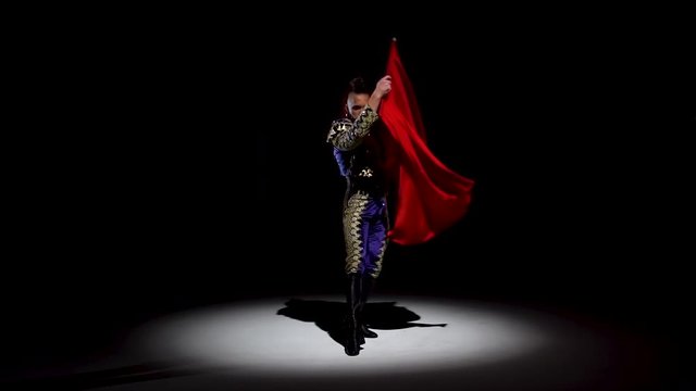 Torero in blue and gold suit or typical spanish bullfighter isolated spotlight on a black background. Close up, slow motion.