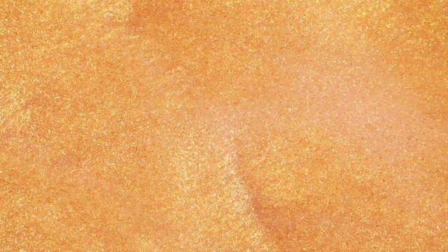 Colorful golden sand organically moves in colorful liquid in macro