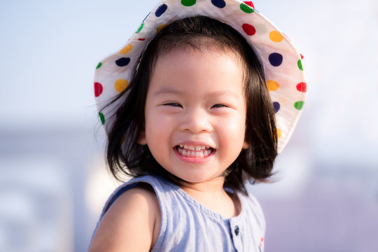 Asian baby child girl beaming smiling. Close up happy face. Little girl wearing white hat. Half body photo. She has tooth decay. Baby age 2 years and 9 month old.