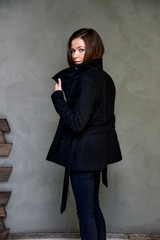 Vertical photo of clothes in a stylish interior in the studio of a glamorous brunette. The girl stands in different poses with long hair on a color fashionable original background.