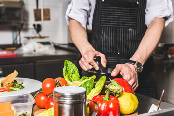 Professional chef cooking in the kitchen restaurant at the hotel, preparing dinner. A cook in an apron makes a salad of vegetables and pizza.