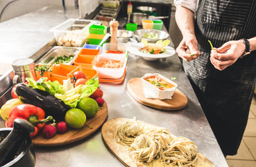 Professional chef cooking in the kitchen restaurant at the hotel, preparing dinner. A cook in an apron makes a salad of vegetables and pizza.