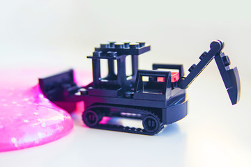 Black toy bulldozer from designer cubes removes pink gel with sparkles inside on a white background close-up 