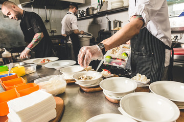 Professional chef cooking in the kitchen restaurant at the hotel, preparing dinner. A cook in an apron makes a salad of vegetables and pizza.