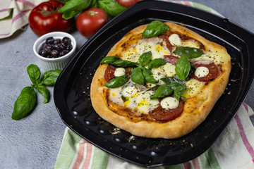 pizza margarita on a baking sheet surrounded by ingredients; tomatoes, basil, olive