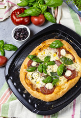 pizza margarita on a baking sheet surrounded by ingredients; tomatoes, basil, olive