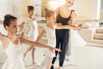 young trainer of the ballet school helps young ballerinas perform different choreographic exercises in studio. children girls rehearse together in the ballet class
