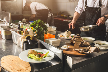 Professional chef cooking in the kitchen restaurant at the hotel, preparing dinner. A cook in an apron makes a salad of vegetables and pizza.