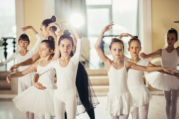 little caucasian girls in white tutu skirts and pointe shoes dream of becoming great ballerinas, training, practicing classic ballet dance in studio, group of little caucasian graceful girls