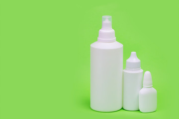 Three white bottles on a green background. Cosmetic kit for skin care. Bottles of different sizes.