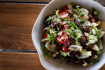 Salad with green and purple lettuce, tomato, croutons and slices of parmesan cheese, olive oil, rustic wooden background