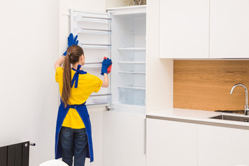 Obraz premium professional cleaning service. Two women in working uniform, in aprons, divide the cleaning of the kitchen of a private house, cottage. washing the refrigerator, tap, sink. Wash floor.
